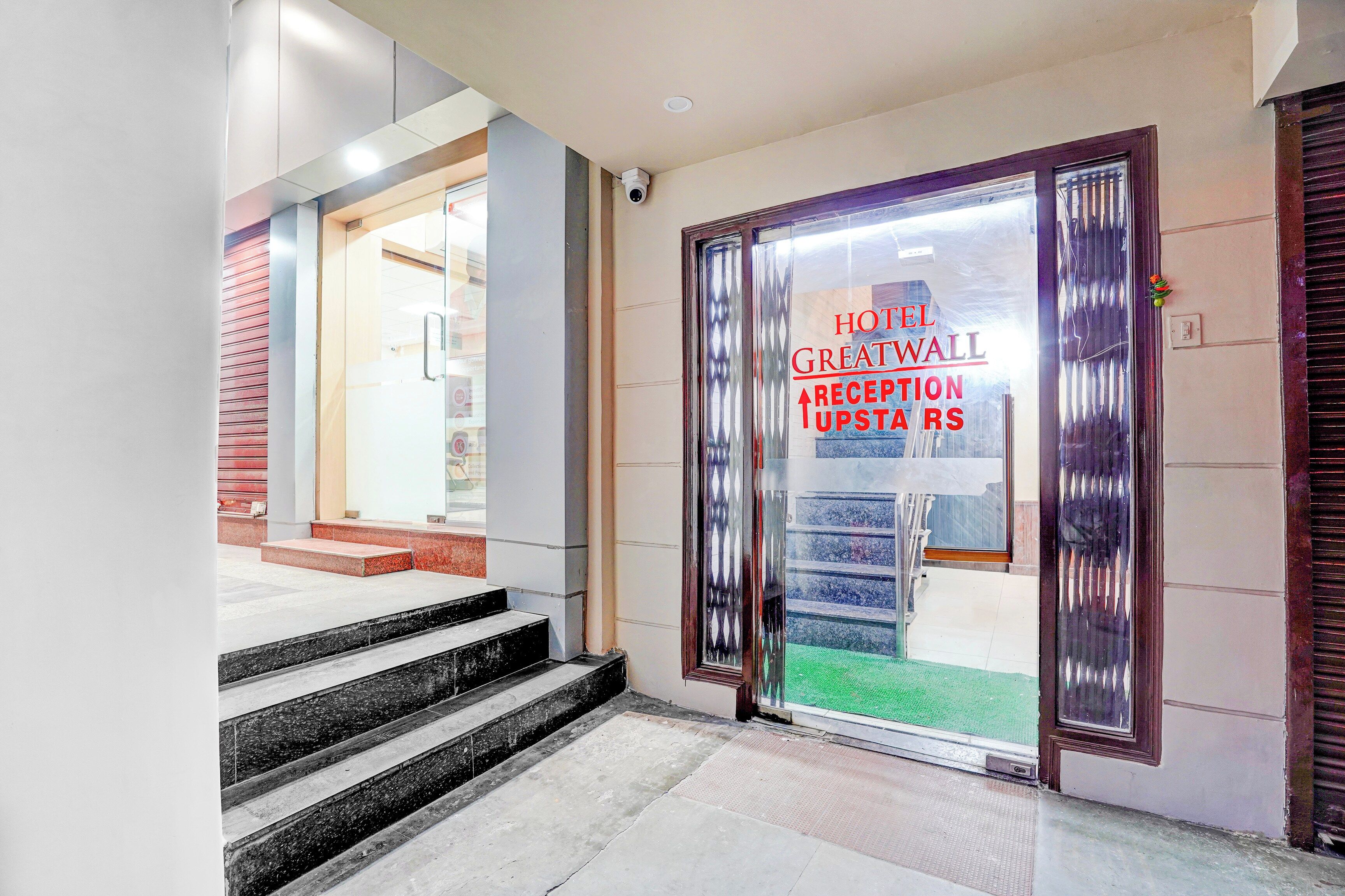 L’entrée d’un hôtel, avec un comptoir d’accueil, un escalier menant aux étages supérieurs et une porte vitrée portant une signalétique.