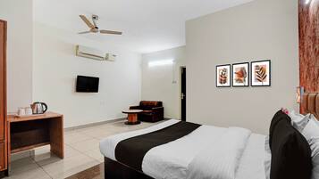 Quarto de hotel com cama, escrivaninha, cadeira, televisão e ventoinha no teto.