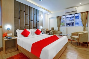 Quarto de hotel com uma cama grande, escrivaninha, cadeira e janela com cortinas.