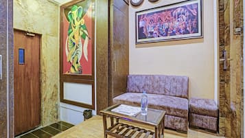 A lobby with a wooden table, a sofa, a painting of an elephant, and a clock on the wall.