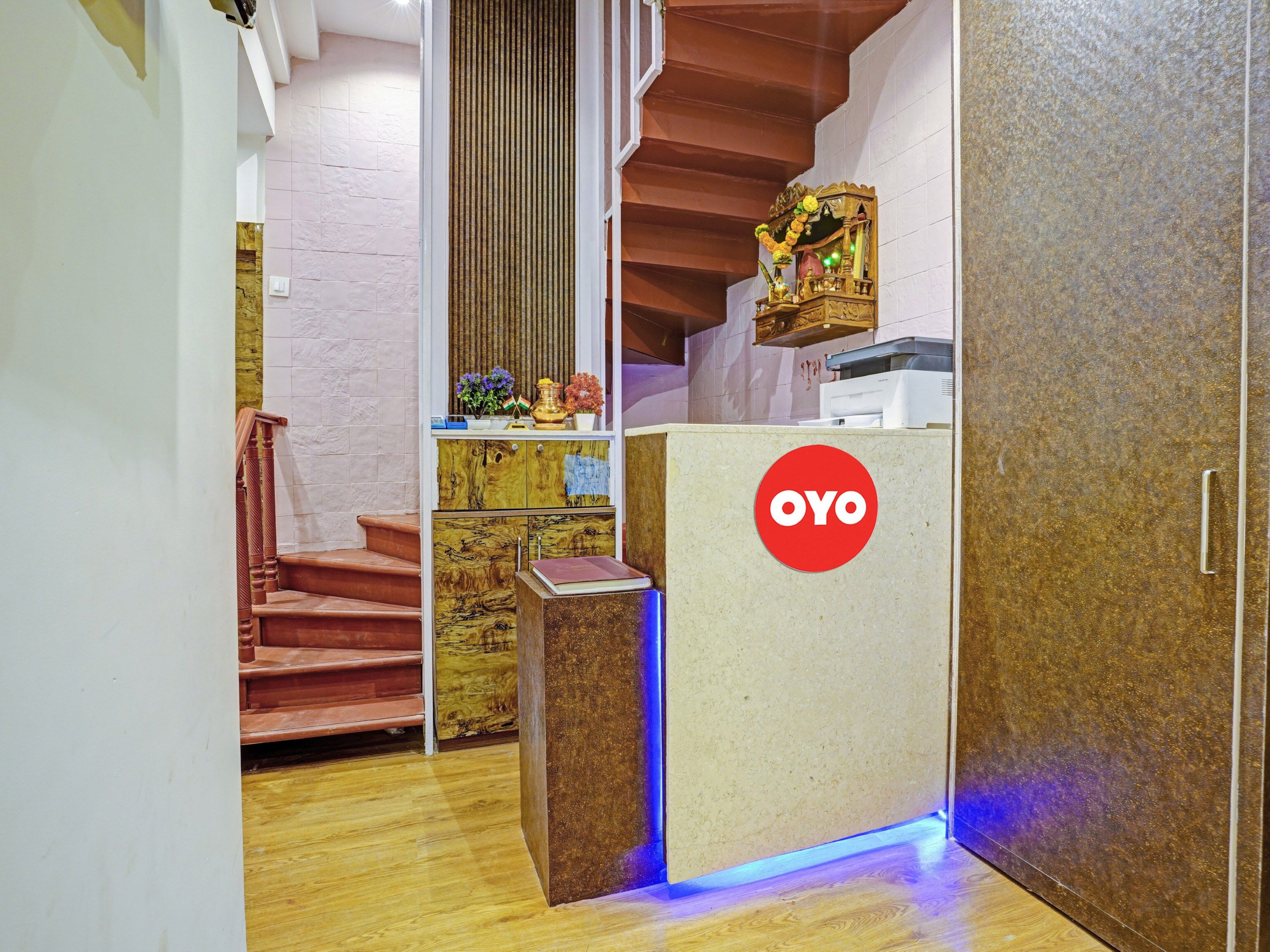 A reception area with a wooden staircase, a reception desk with a logo, and a wall-mounted shelf with decorative items.