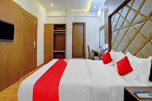 Quarto de hotel com uma cama grande, televisão, guarda-roupa e secretária com cadeira.