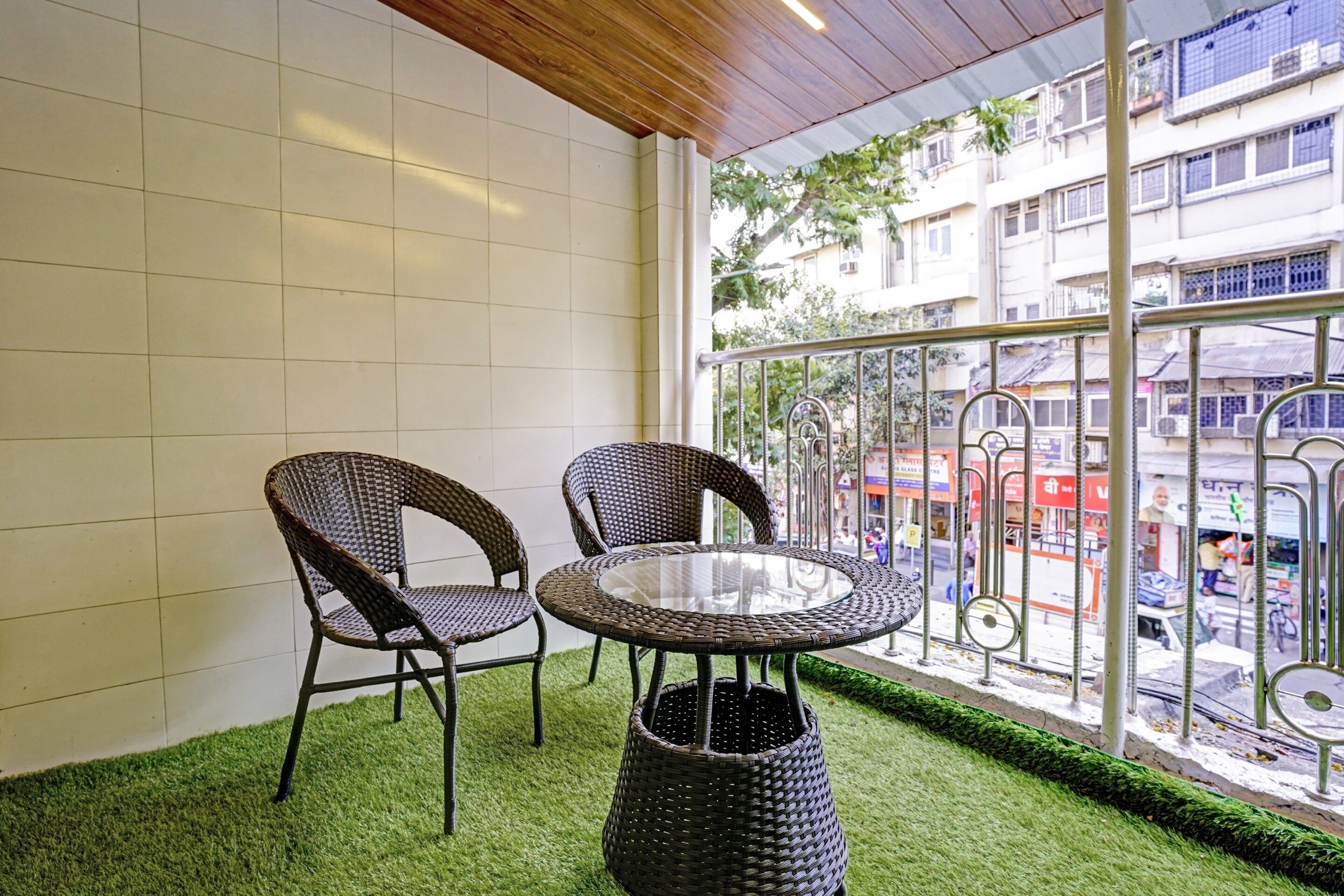 A room with two wicker chairs and a glass table, a small woven basket, and a view of a street through a metal railing.