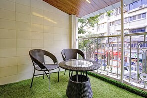 A room with two wicker chairs and a glass table, a small woven basket, and a view of a street through a metal railing. - Hotel O Sunrise Suites (Mumbai)