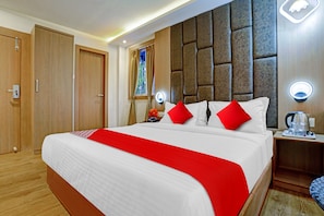 Quarto de hotel com uma cama grande, guarda-roupa de madeira, mesa de cabeceira com cafeteira e janela com cortinas.