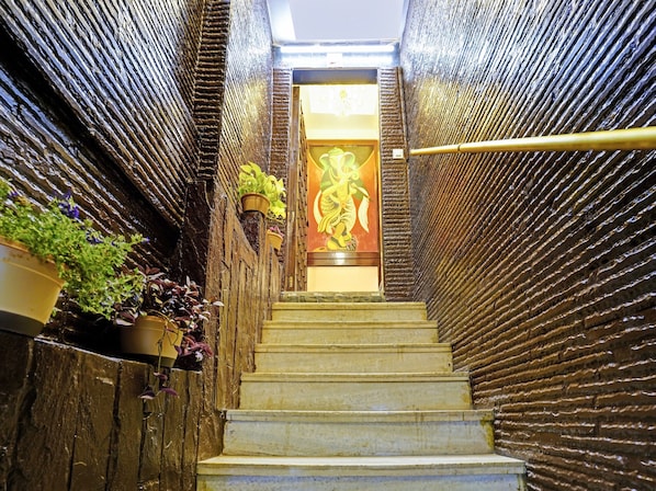 Una escalera con paredes texturizadas a cada lado, que conduce a una puerta con un panel decorativo.
