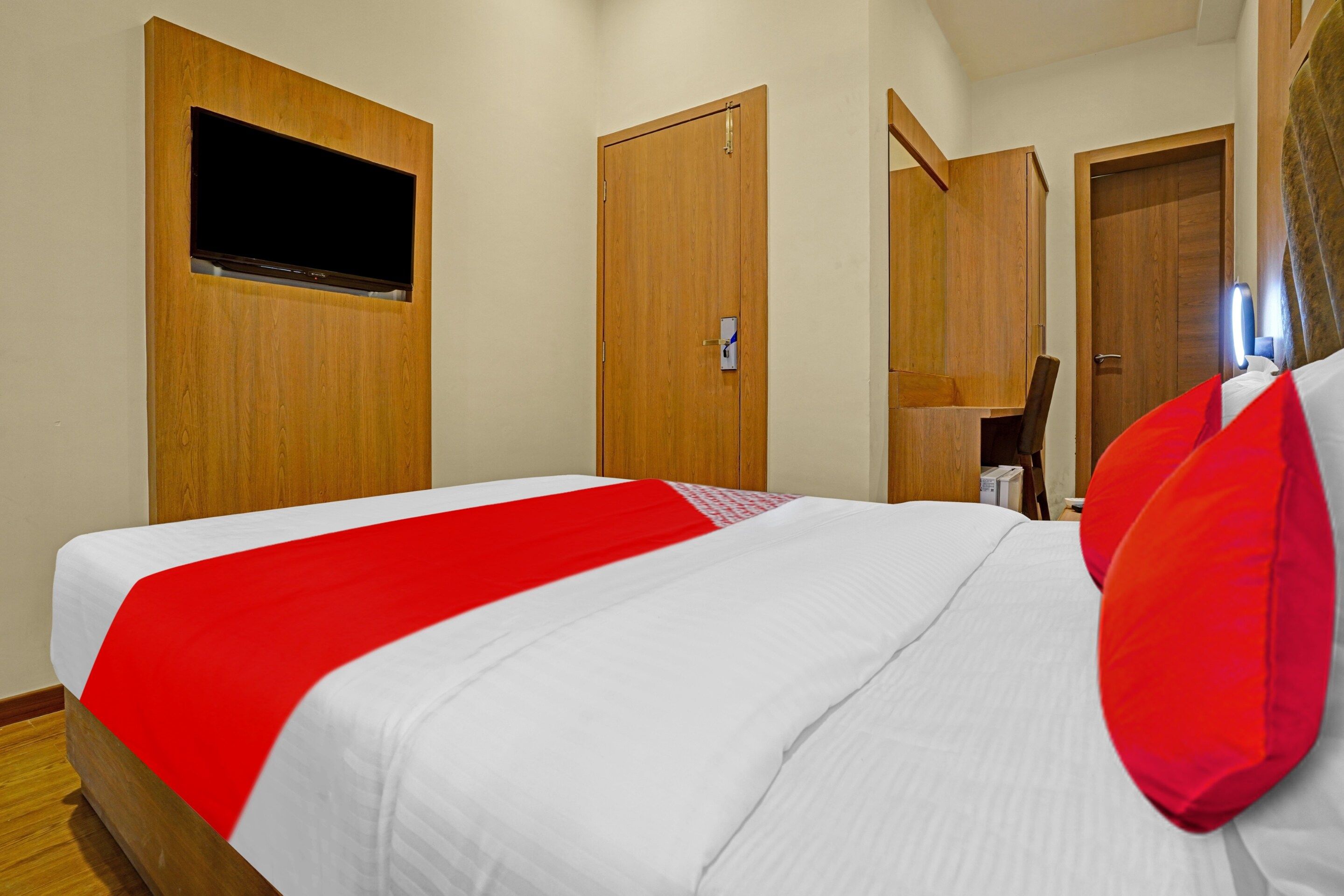 A hotel room with a bed, a television mounted on the wall, and wooden doors.