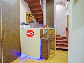 Uma área de recepção com balcão da marca 'OYO', uma escada e uma estante decorativa com flores.