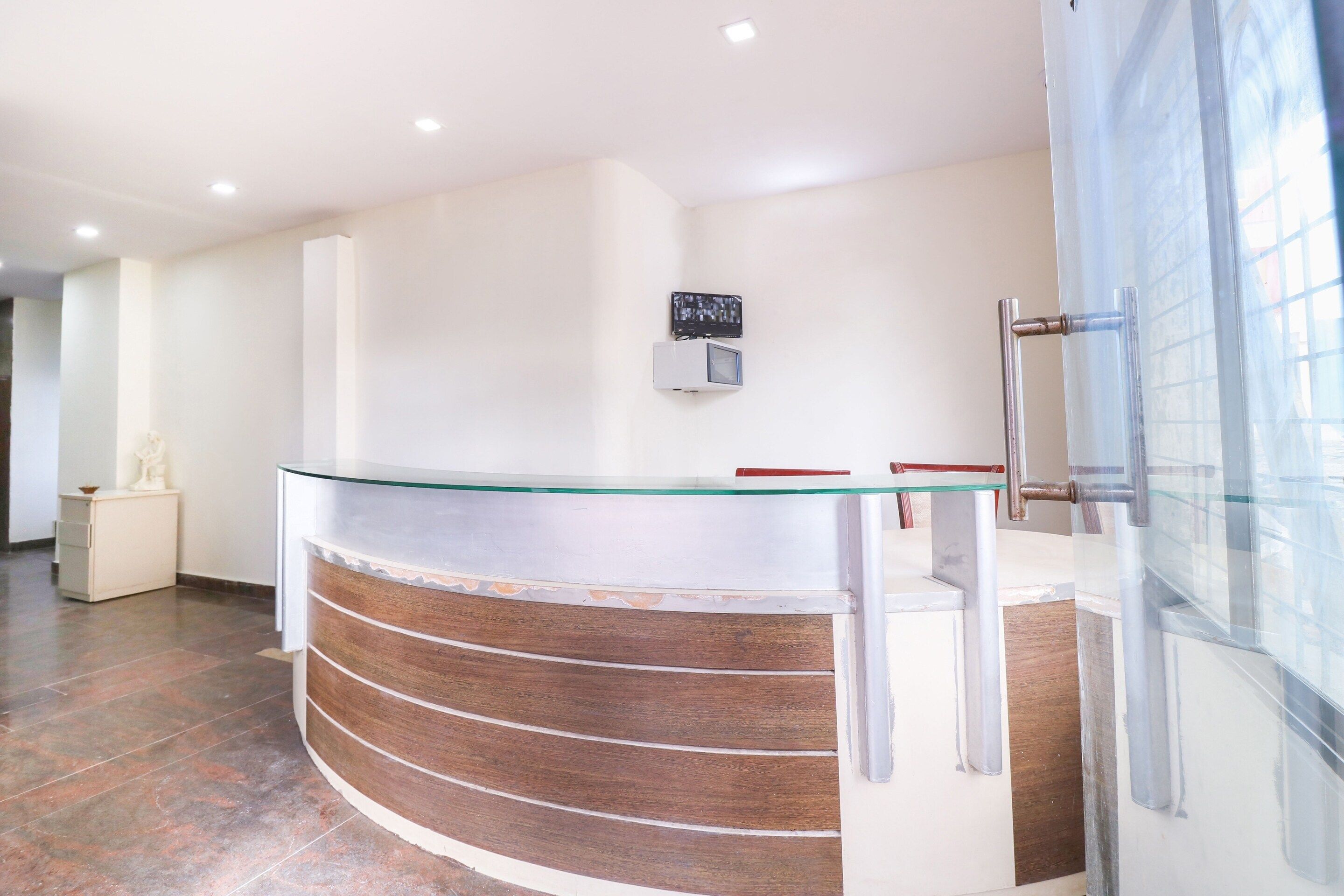 A reception desk with a glass top and wooden paneling, a wall-mounted television, and a door with a glass panel.