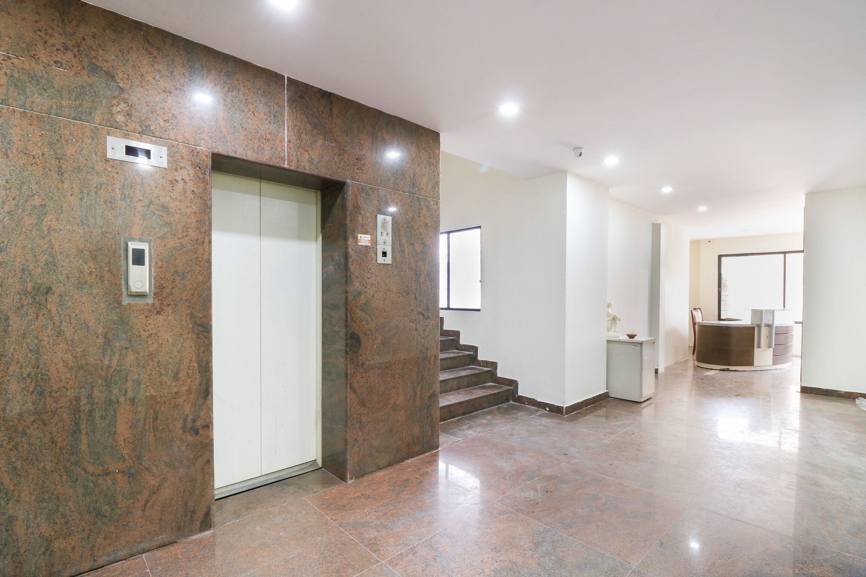 Un interior moderno con pared de mármol, un ascensor, una escalera y una zona de recepción.