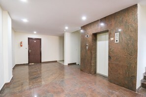 Um corredor com piso de mármore, uma porta e um elevador.