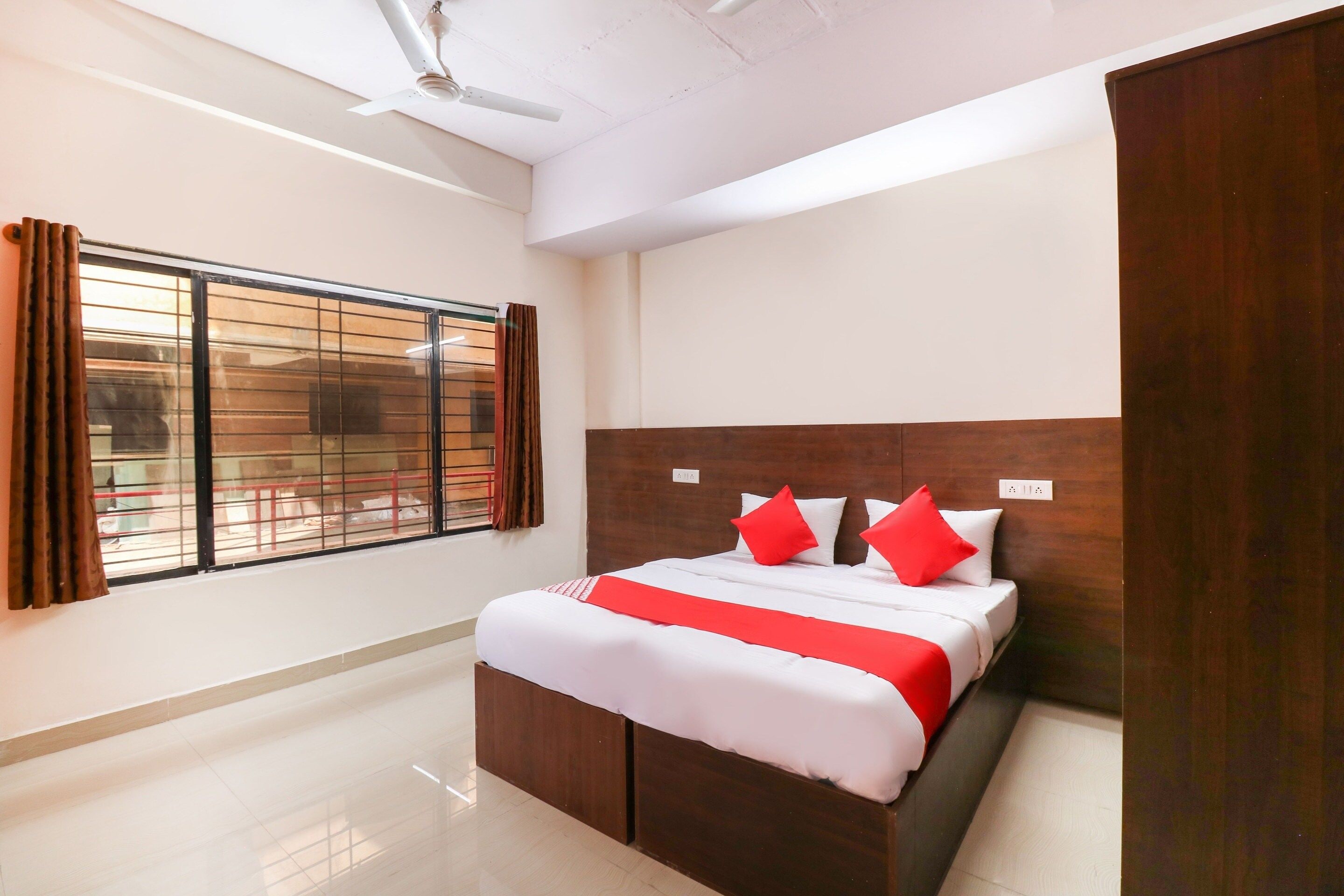 Una habitación de hotel con cama, ventana con cortinas, ventilador de techo y cabecero de madera.
