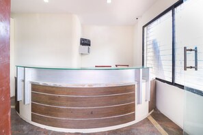 Uma mesa de recepção com tampo de vidro, painéis de madeira e um ar condicionado fixado na parede.