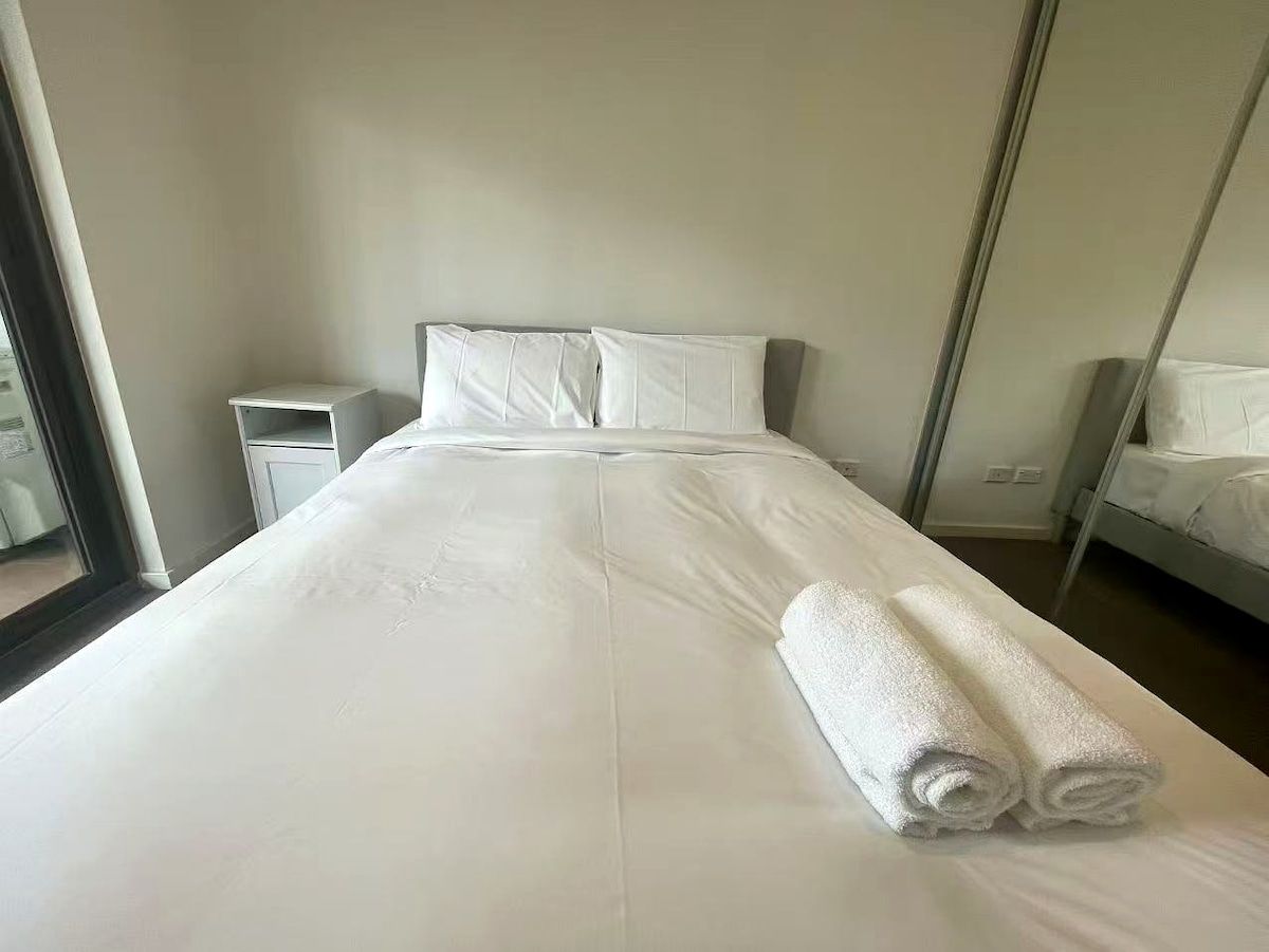 A hotel room with a large bed, a nightstand, a mirror, and a window.