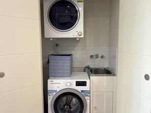 A compact laundry area with a front-loading washing machine, a dryer, and a small sink. - Stylish Modern Retreat in Ermington (Ermington)