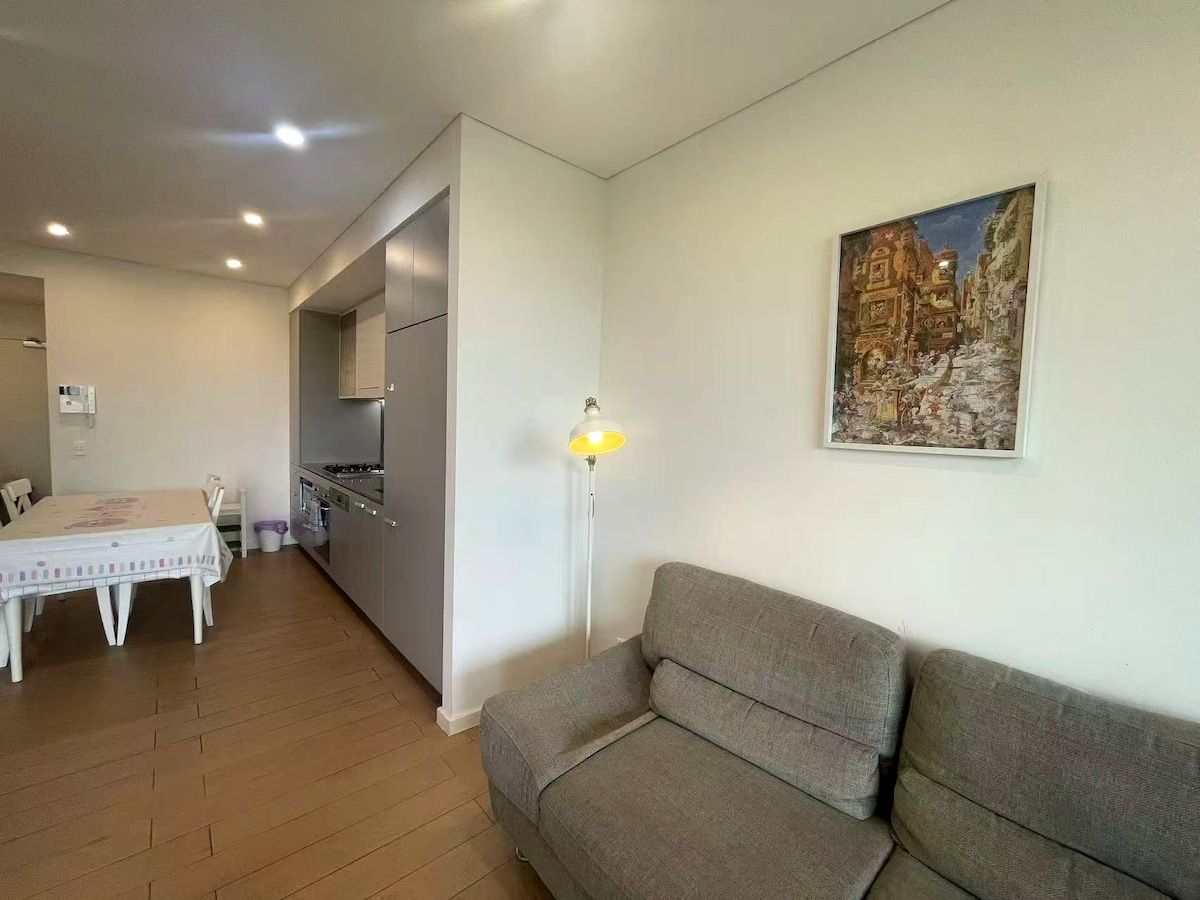 A living room with a sofa, a dining table, and a kitchen area.