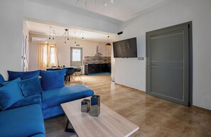 A modern living room with a blue sofa, a coffee table, and a TV mounted on the wall. - Loulaki Villas Santorini by MPS (vourvoulos)