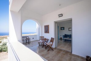 A balcony with a table and chairs, a view of the sea, and a doorway leading to an interior space with a sofa. - Loulaki Villas Santorini by MPS (vourvoulos)