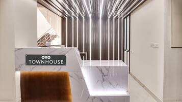 Una zona de recepción con mostrador de mármol, un letrero que dice 'OYO TOWNHOUSE' y una escalera al fondo.