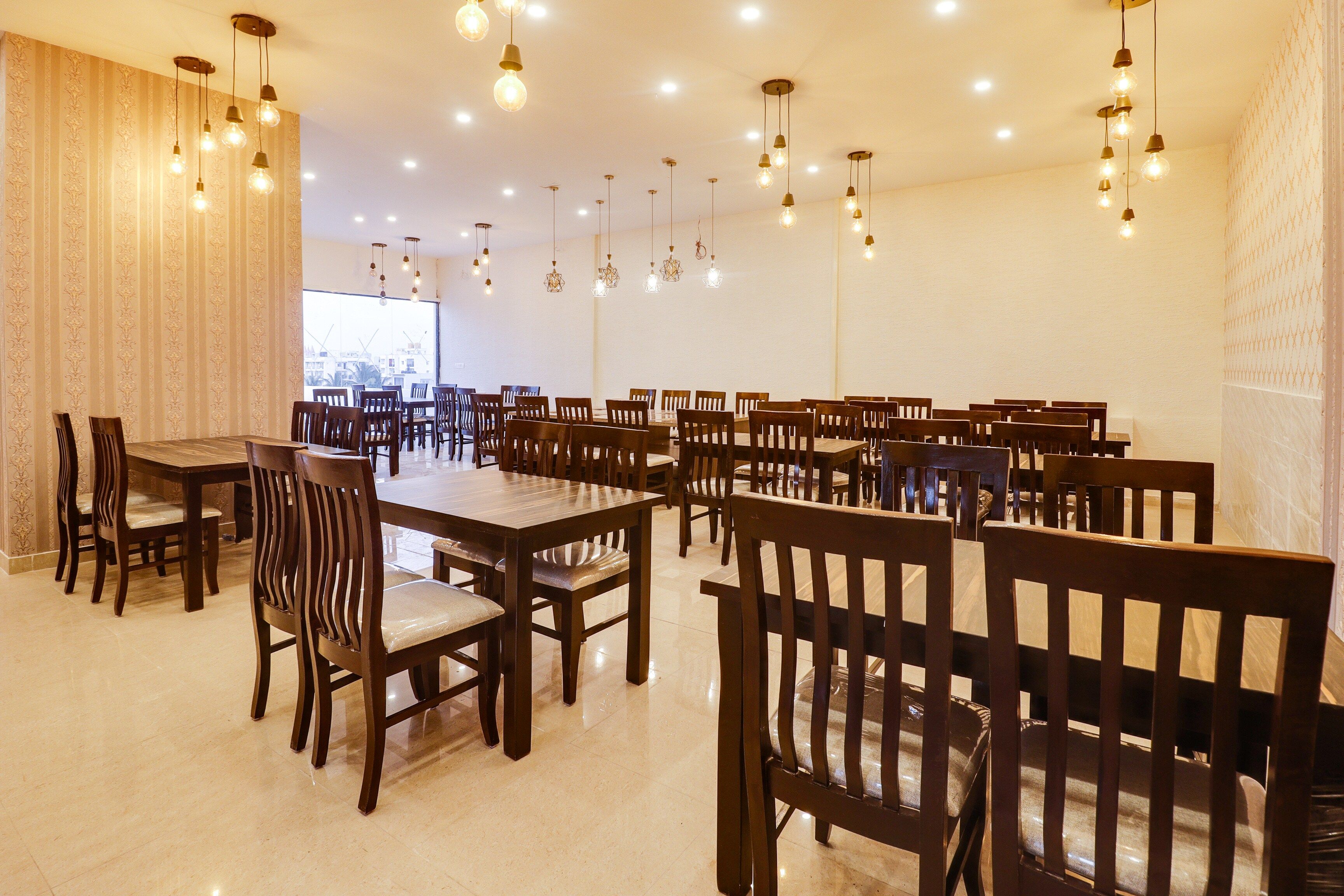 Un comedor amplio con múltiples mesas y sillas, iluminación en el techo y vistas a edificios.