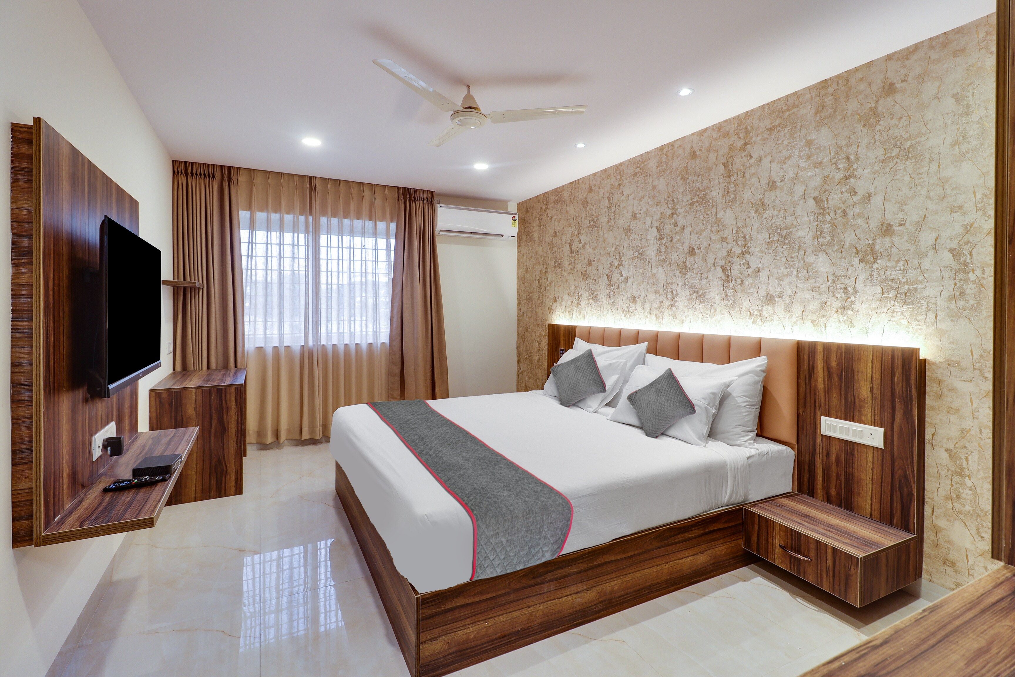 Habitación de hotel con cama, mesitas de noche, televisor, ventilador de techo y aire acondicionado.