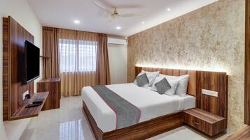 Habitación de hotel con cama, mesitas de noche, televisor, ventilador de techo y aire acondicionado.