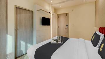A hotel room with a bed, a television mounted on the wall, and a tray with a kettle and cups on the bed.