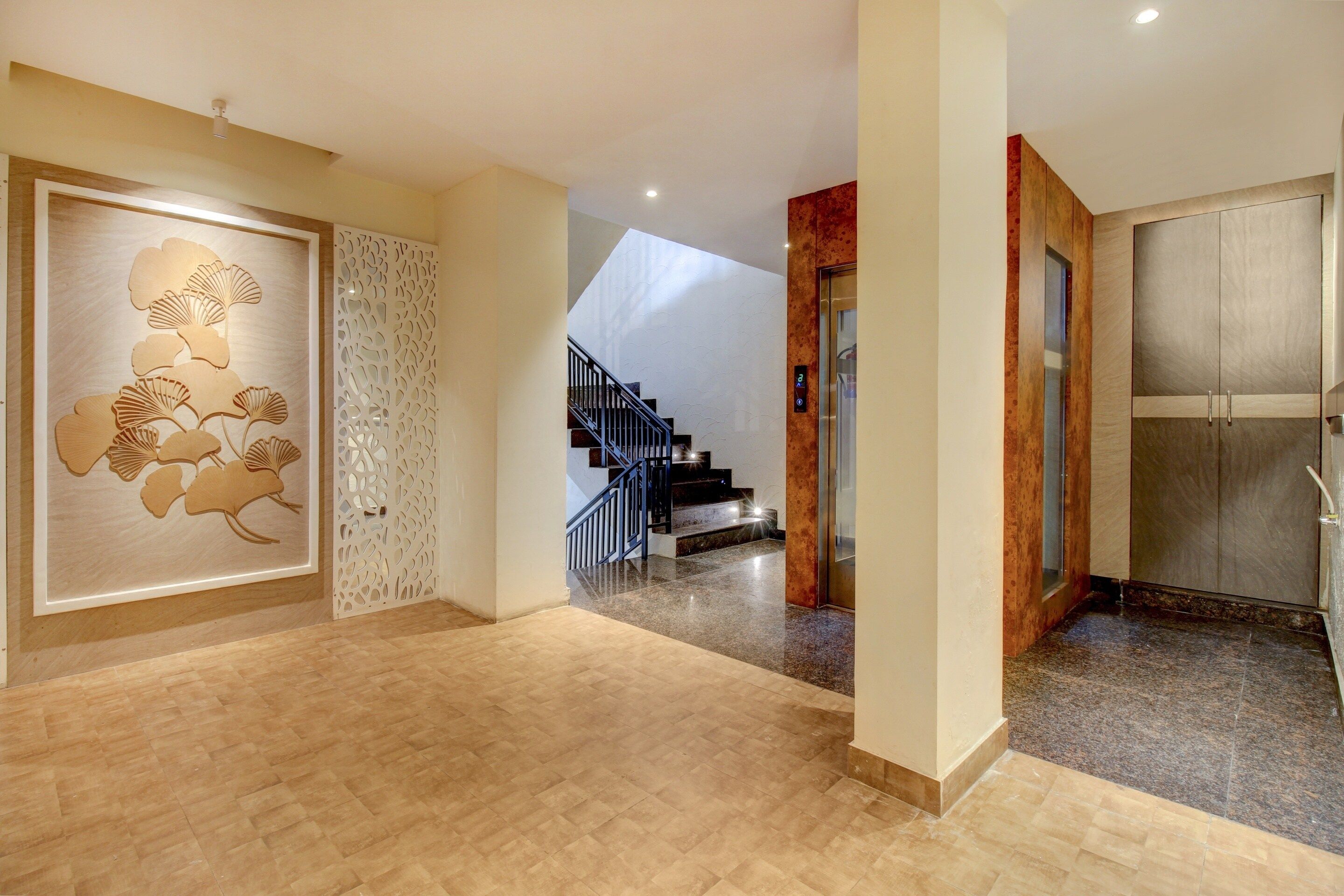 Un pasillo espacioso con suelo de madera, un panel decorativo con motivos de hojas, una escalera con barandilla metálica y una puerta con un panel de vidrio esmerilado.