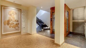 Un pasillo espacioso con suelo de madera, un panel decorativo con motivos de hojas, una escalera con barandilla metálica y una puerta con un panel de vidrio esmerilado.