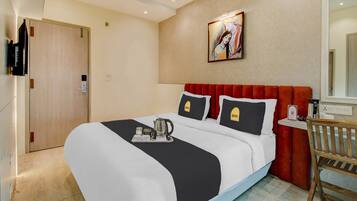 Habitación de hotel con una cama, un cuadro en la pared, una puerta de madera y una mesita con una tetera y tazas.