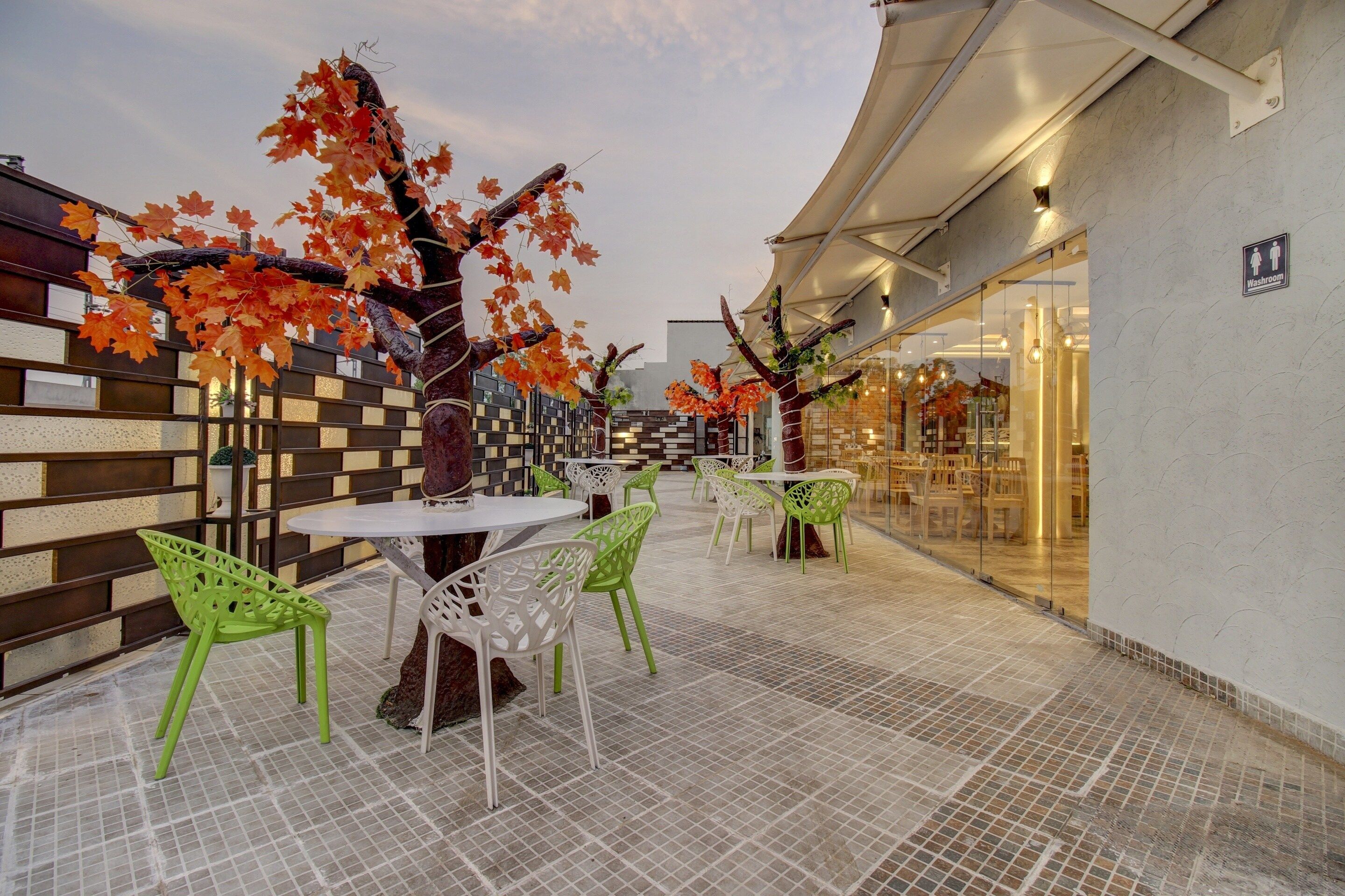 An outdoor seating area with tables and chairs, a tiled floor, and a building entrance with a sign indicating a washroom.