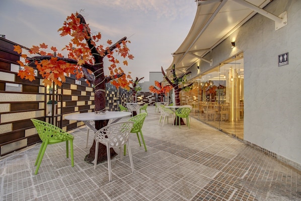 An outdoor seating area with tables and chairs, a tiled floor, and a building entrance with a sign indicating a washroom.