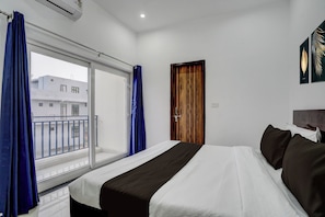 Una habitación de hotel con una cama, un ventanal con cortinas, una puerta y vistas a edificios.