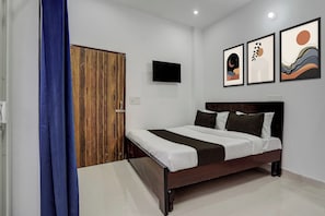 Un dormitorio con un armario de madera, una cama con ropa de cama blanca y marrón, y tres obras de arte enmarcadas en la pared.