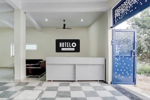 Zona de recepción de un hotel con cartel que indica servicio para empresas, un ventilador de techo, mostrador de recepción y una puerta azul con diseño geométrico.