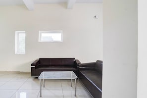 Una habitación con un sofá de cuero marrón oscuro, una mesa de centro de cristal y dos ventanas.