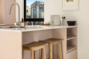 A modern kitchen with a built-in sink, a window with a city view, a coffee machine, and wooden stools. - Beautifully Furnished 1-Bed in the City Centre (Christchurch)