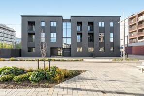 A modern two-story building with a flat roof, large windows, and a paved courtyard with plants. - Beautifully Furnished 1-Bed in the City Centre (Christchurch)