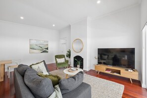 A modern living room with a grey sofa, a green armchair, a flat-screen TV, and a fireplace. - Three-Bed Vic Park Haven (Victoria Park)