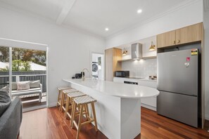 A modern kitchen with a central island, bar stools, a built-in oven, and a stainless steel refrigerator. - Three-Bed Vic Park Haven (Victoria Park)
