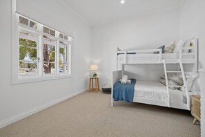 A room with a bunk bed, a small table with a lamp, and a window with a view of trees and a white fence. - Three-Bed Vic Park Haven (Victoria Park)