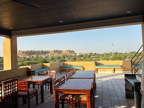 Un patio exterior con asientos y mesas, con vistas a un paisaje urbano que incluye una colina y edificios.