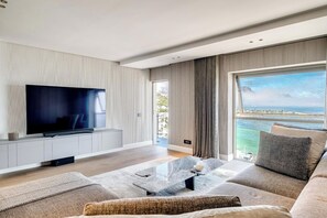 A modern living room with a flat-screen TV, a sofa, a coffee table, and a view of the sea. - Clifton 2 Bed Apartment Ocean Views Dunmore Noir (Cape Town)