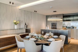 A modern dining area with a central table set for four, surrounded by white chairs. - Clifton 2 Bed Apartment Ocean Views Dunmore Noir (Cape Town)