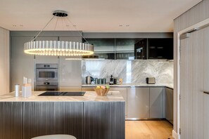 Une cuisine moderne dotée d’un îlot central, d’appareils électroménagers en acier inoxydable et d’un dosseret en marbre.