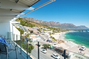 A balcony with a view of a coastal town, a beach, and mountains. - Clifton 2 Bed Apartment Ocean Views Dunmore Noir (Cape Town)