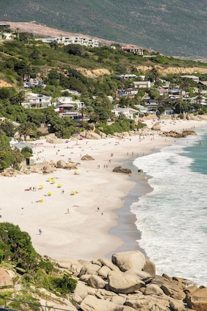 A coastal beach with rocky terrain and a variety of buildings in the background. - Clifton 2 Bed Apartment Ocean Views Dunmore Noir (Cape Town)