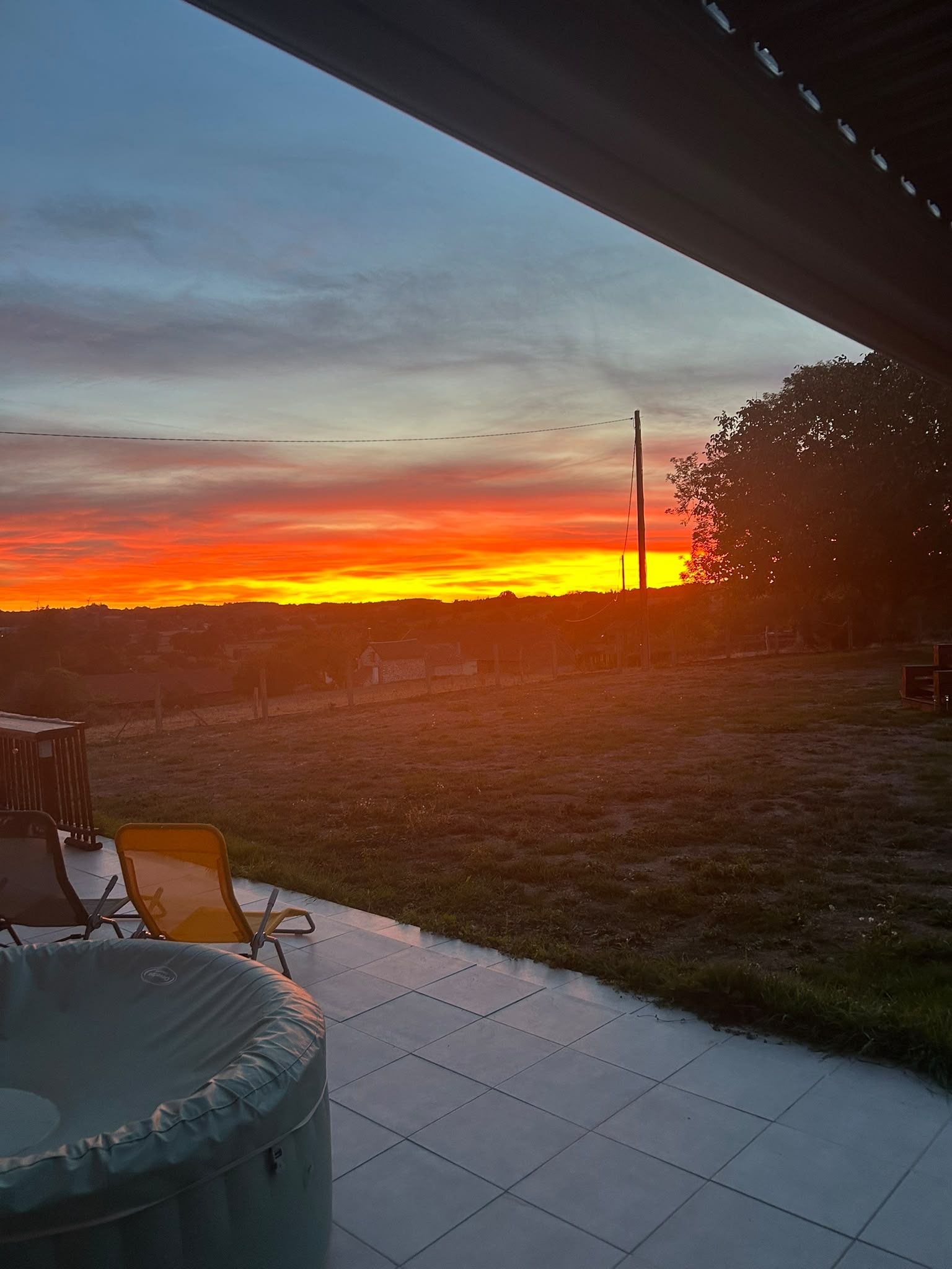 Un espace extérieur aménagé en terrasse, offrant une vue sur un coucher de soleil se déclinant sur un paysage rural.