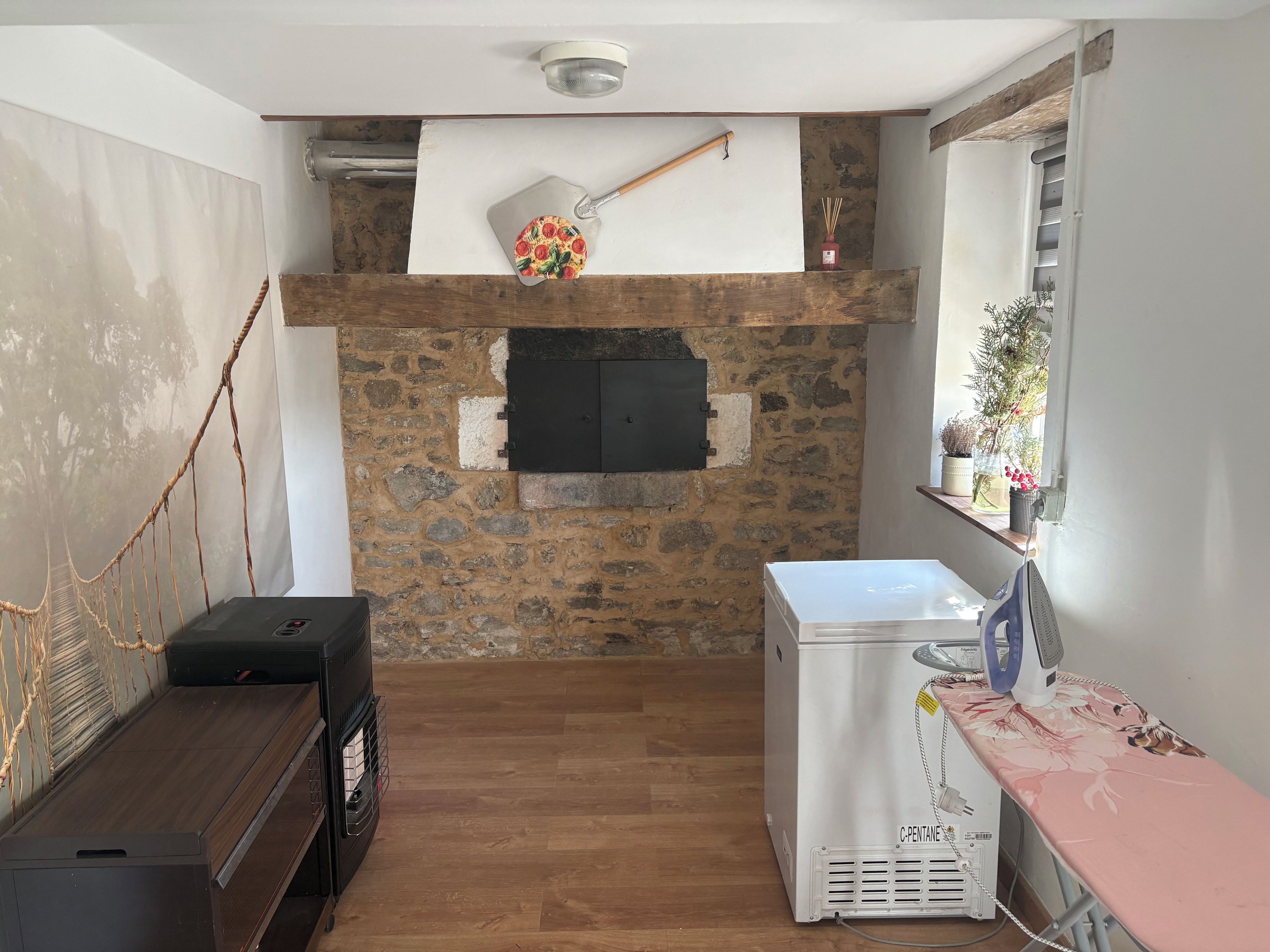 Une pièce avec un mur en pierre, une cheminée, un banc en bois, un appareil électroménager blanc et une fenêtre ornée de plantes.