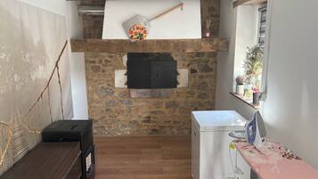 Une pièce avec un mur en pierre, une cheminée, un banc en bois, un appareil électroménager blanc et une fenêtre ornée de plantes.